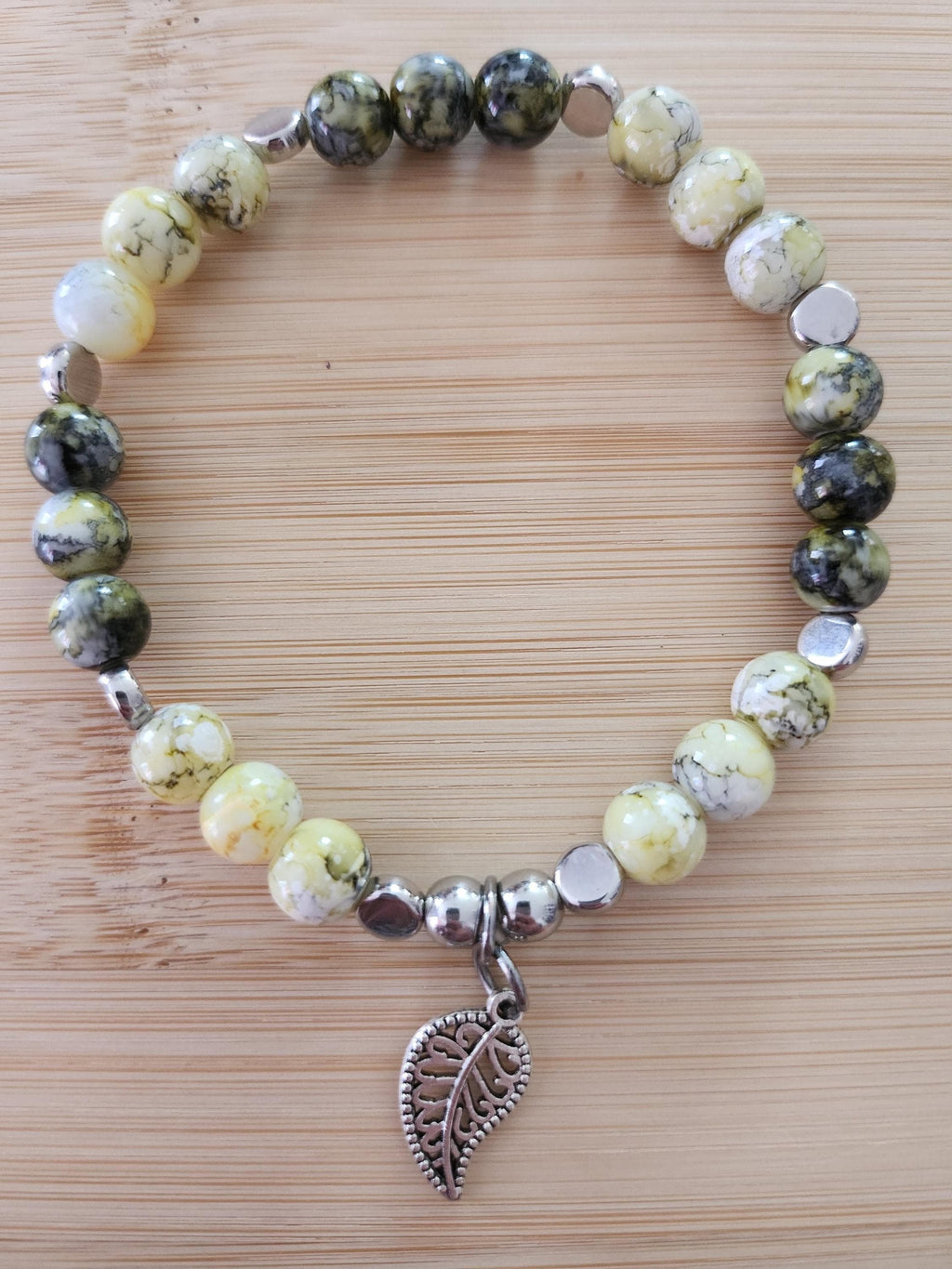 Bracelet en perles vertes, jaunes et grises, intercalaires argentés et breloque feuille