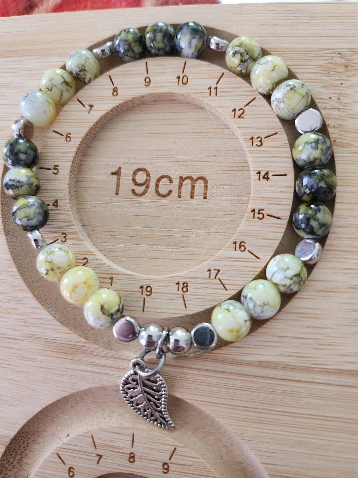 Bracelet en perles vertes, jaunes et grises, intercalaires argentés et breloque feuille